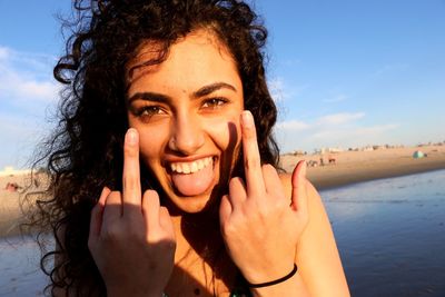 Close-up portrait of cheerful young woman showing obscene gesture at beach