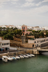 Boats moored on river by buildings in city against sky