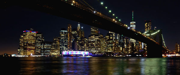 Illuminated buildings by river against sky at night