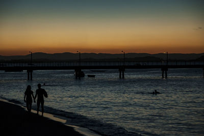 Silhouette people on sea against sky during sunset