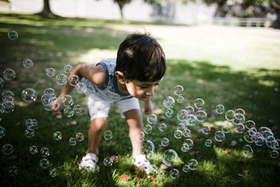 High angle view of boy playing with bubbles while standing on grassy field at park