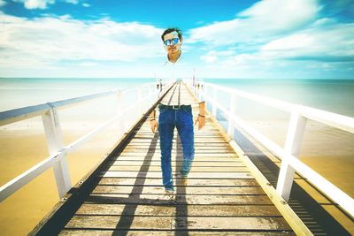 Man standing on railing by sea against sky