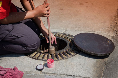 Midsection of person repairing manhole on sidewalk