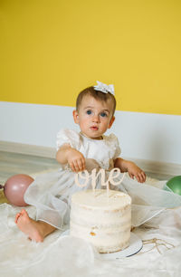 Cute baby girl sitting by cake at home