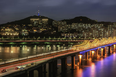 Illuminated bridge over river amidst buildings in city at night