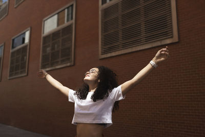 Carefree woman with arms outstretched by building