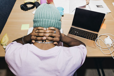 Rear view of tired sitting with hands behind neck in college dorm