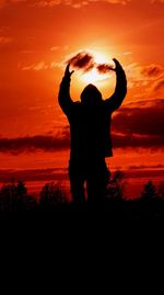 Silhouette man standing on field against orange sky