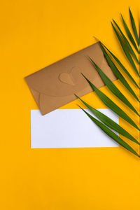 Flat lay with empty greeting card with envelope and palm branch on yellow background