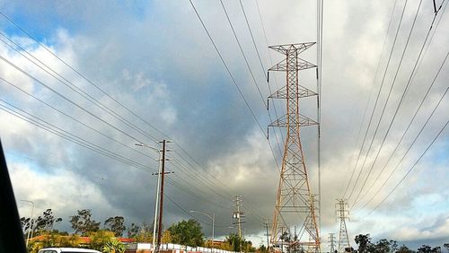 Low angle view of electricity pylon against cloudy sky