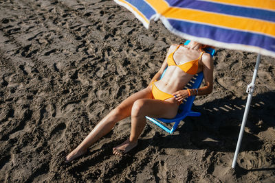 Anonymous young redhead woman sitting on chair at beach on a sunny day in summer