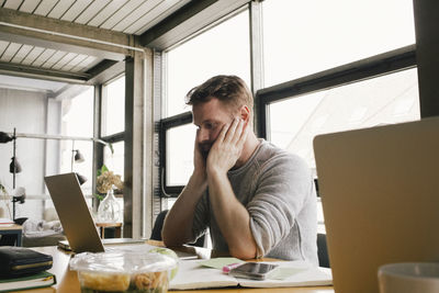 Confused businessman sitting with head in hands looking at laptop on desk