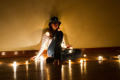 Young woman sitting on floor against illuminated wall