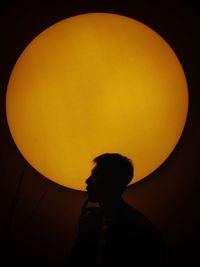 Silhouette man looking at illuminated lamp against sky at sunset