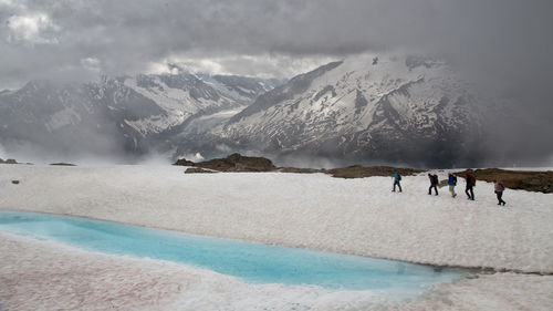 People walking on snow covered hill against cloudy sky