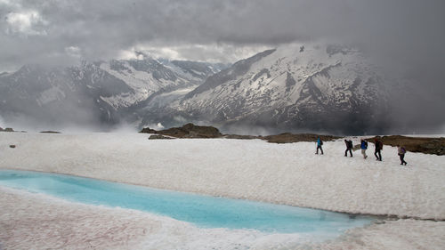 People walking on snow covered hill against cloudy sky