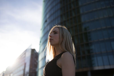 Side view of beautiful young woman standing against buildings in city
