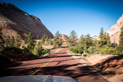 Road leading towards mountains against clear blue sky