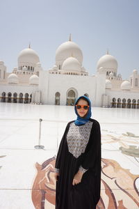 Portrait of young woman standing against mosque and clear sky