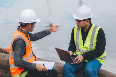 Rear view of two man using digital tablet while sitting at lake