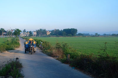 People riding bicycle on road amidst field against clear sky