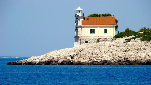 Lighthouse by sea against buildings against clear sky