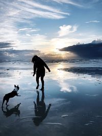 Silhouette woman running with dog at beach during sunset