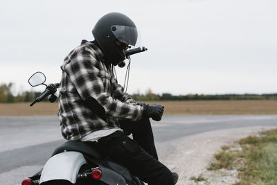 Man sitting on motorcycle at roadside against sky