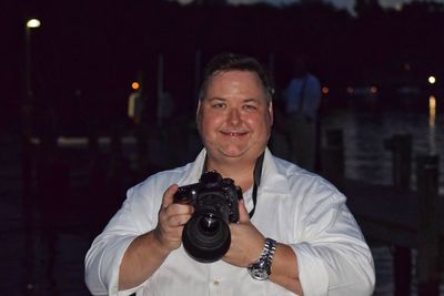 Portrait of smiling man holding camera at night
