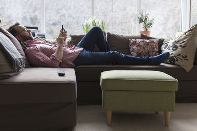 Mature mna lying on couch checking messages on smart phone