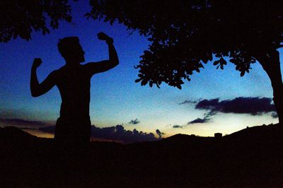 Silhouette man with arms raised against sky during sunset