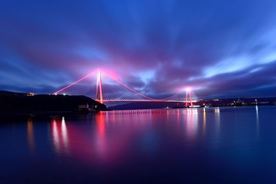 Illuminated bridge over river against sky at night