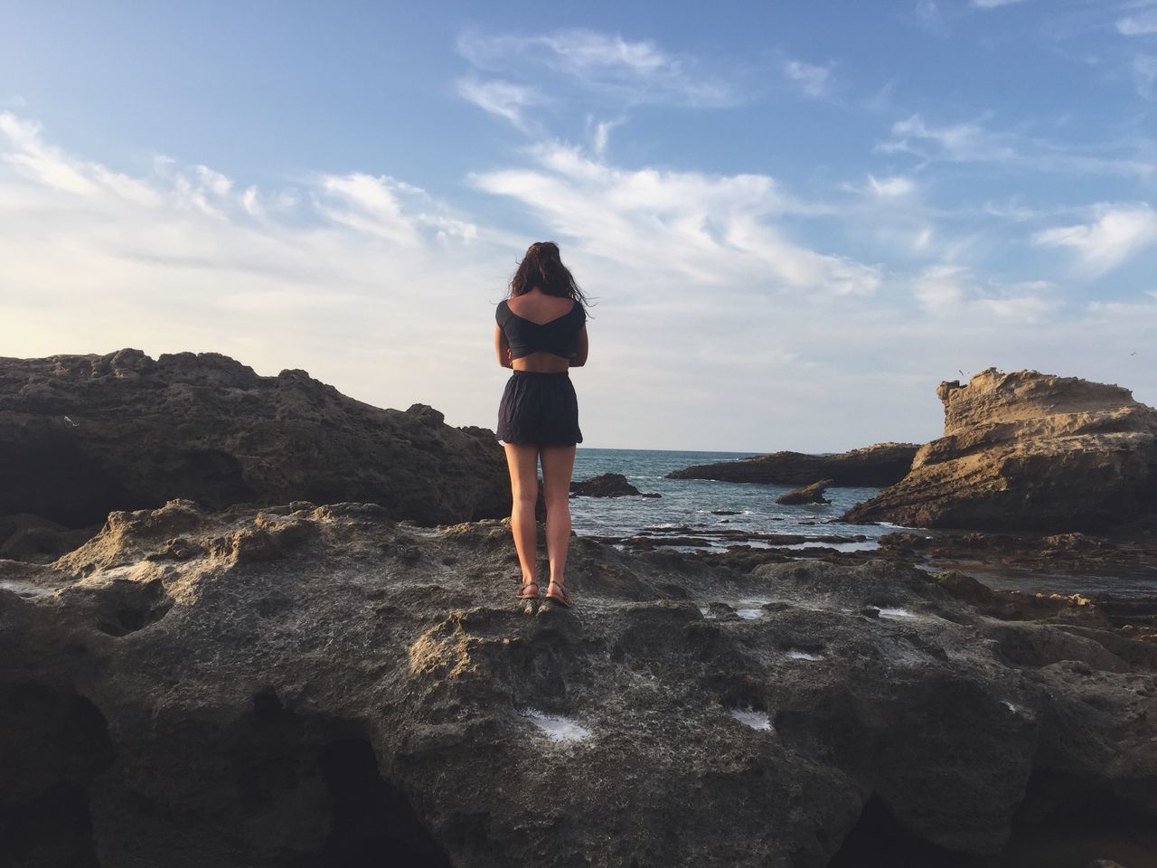 full length, lifestyles, standing, leisure activity, sky, rear view, tranquil scene, tranquility, scenics, beauty in nature, sea, casual clothing, water, rock - object, nature, beach, getting away from it all, shore