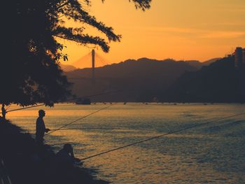 Silhouette man fishing by sea against sky during sunset