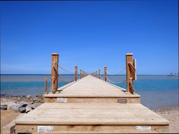 Pier over sea against clear blue sky