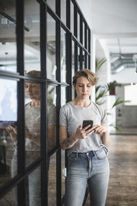 Female entrepreneur using smart phone by wall at creative office