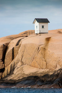 Hut on rock formation at sea shore against sky