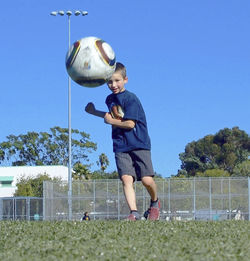 Boy playing with ball on field against clear sky
