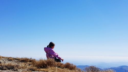 Full length of girl sitting on land against clear sky