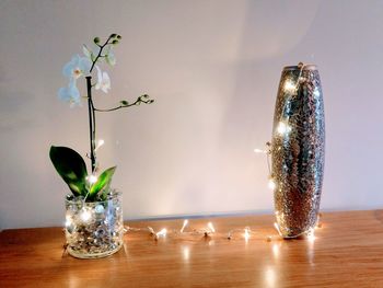 Close-up of illuminated vase on table against wall