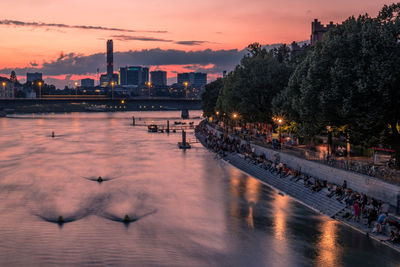 River by illuminated buildings against sky at sunset