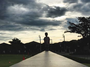 Boy standing by tree in city against sky