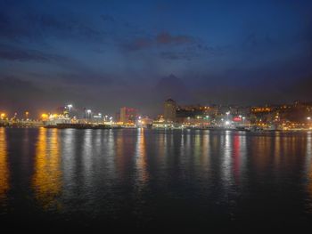 Illuminated buildings by river against sky at night
