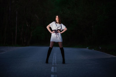 Portrait of young woman standing on road against trees