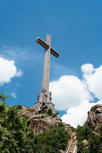 Low angle view of cross on rock against blue sky during sunny day