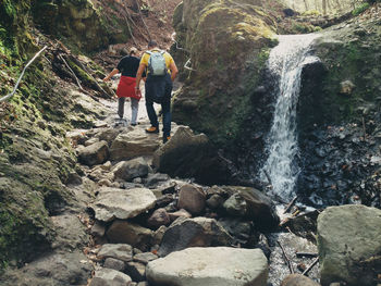 Rear view of people walking by waterfall in forest