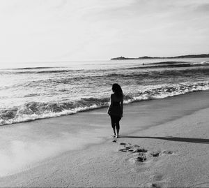 Rear view of silhouette mid adult woman standing at beach against sky