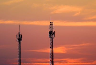 Low angle view of repeater towers against orange sky