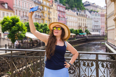 Cheerful woman doing selfie while standing on bridge