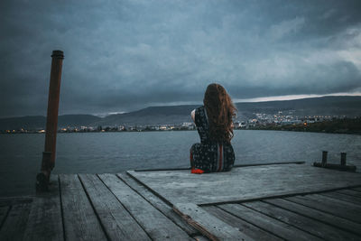 Rear view of woman sitting on pier over river at dusk